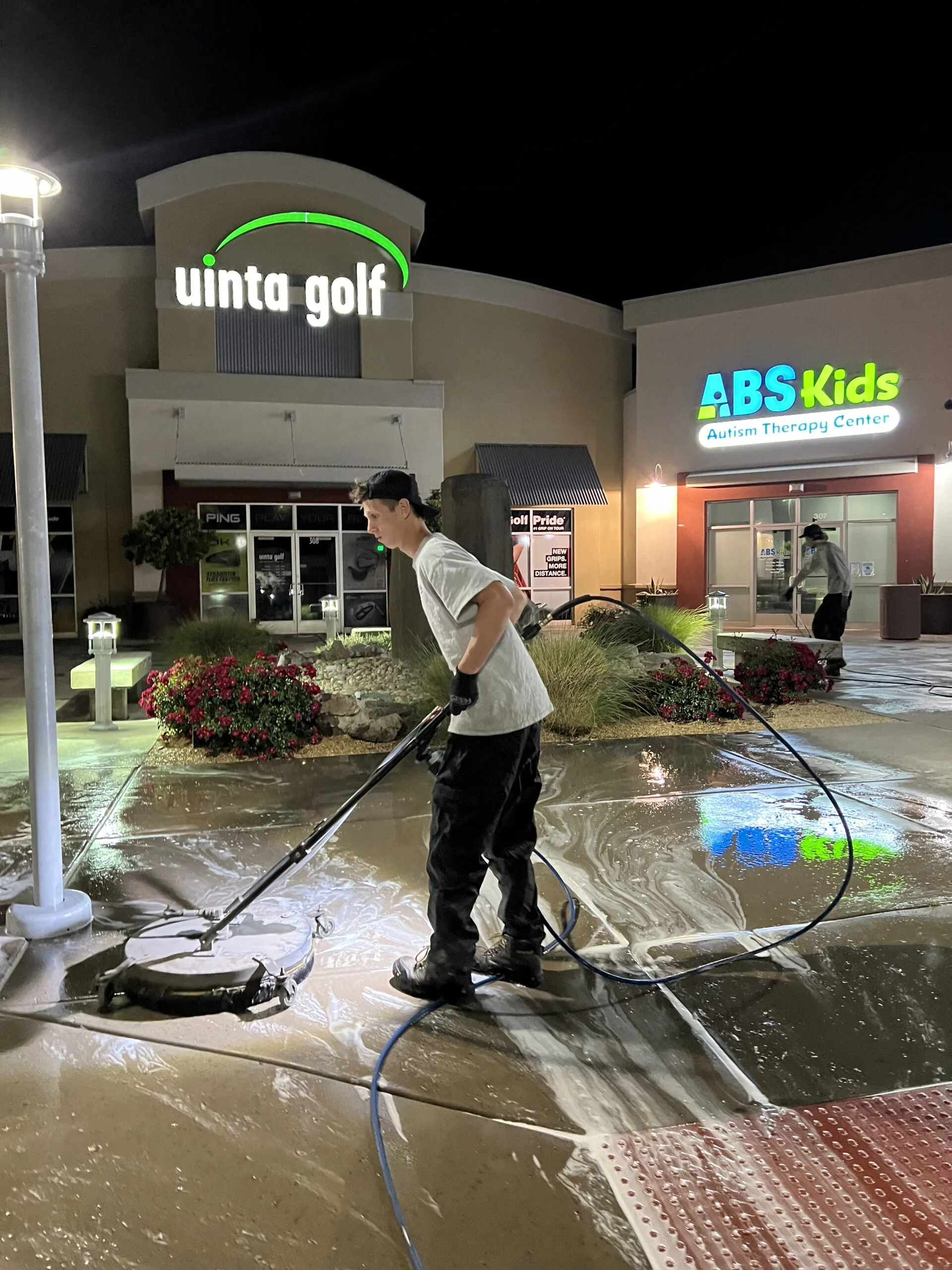 Technician operating a circular surface cleaner on a commercial plaza at night