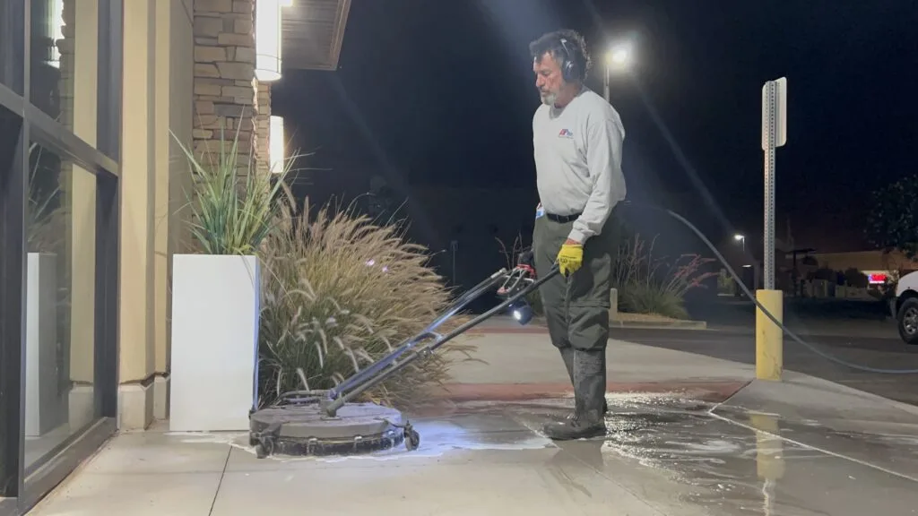 Technician using a surface cleaner on a commercial sidewalk at night