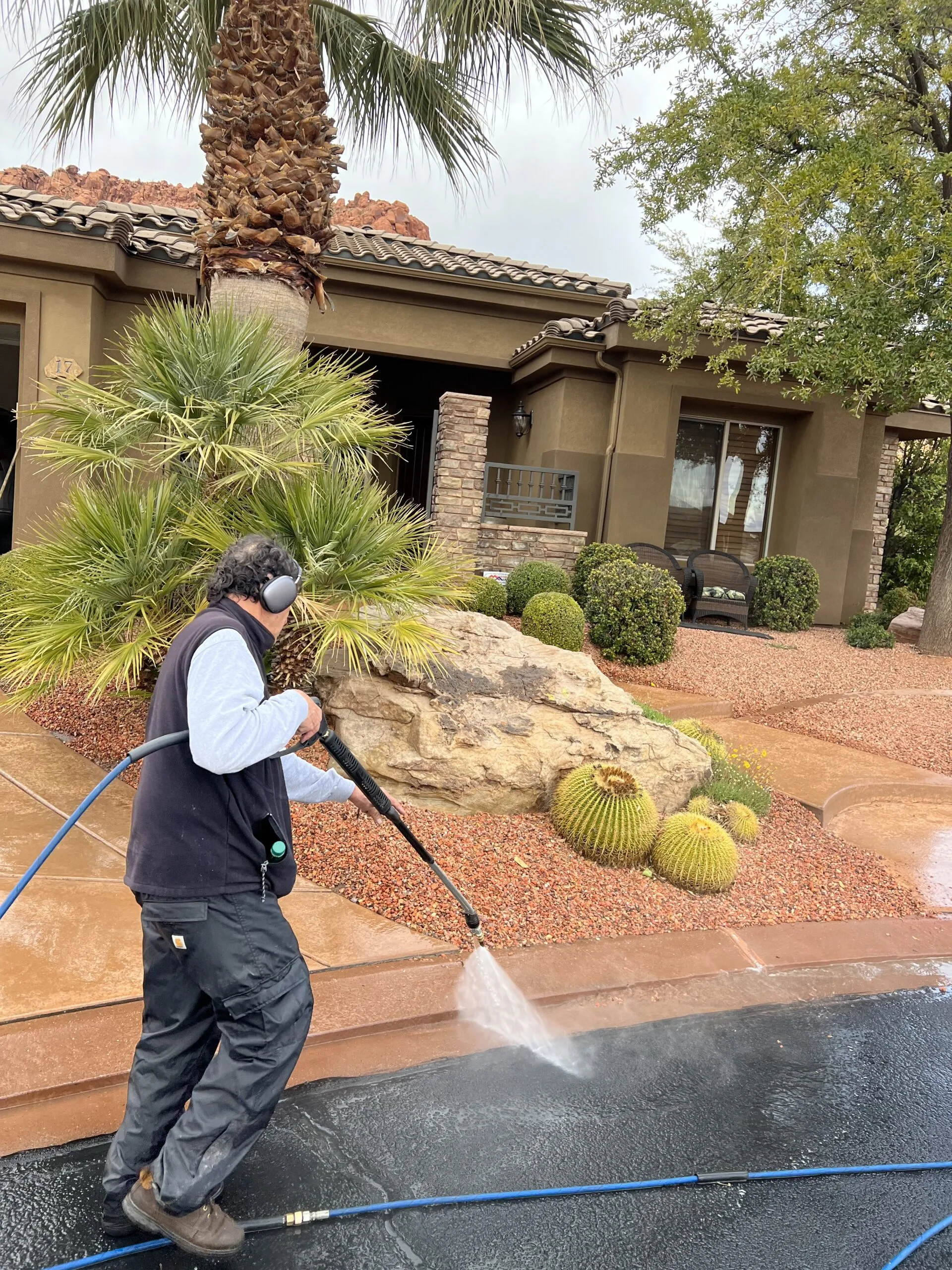 Technician pressure washing a concrete curb beside a residential driveway