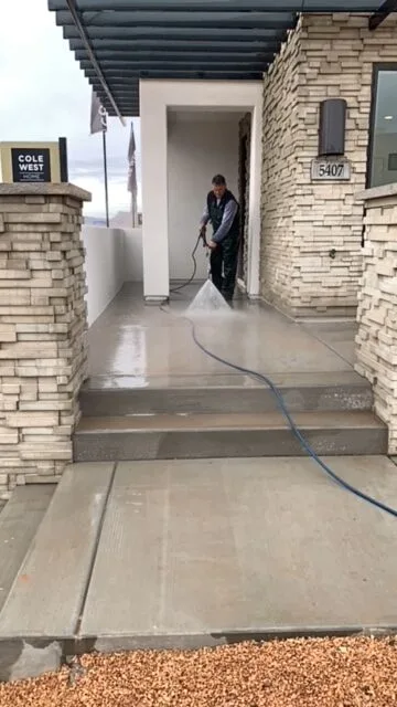 Technician pressure washing concrete steps and landing at a residential entry