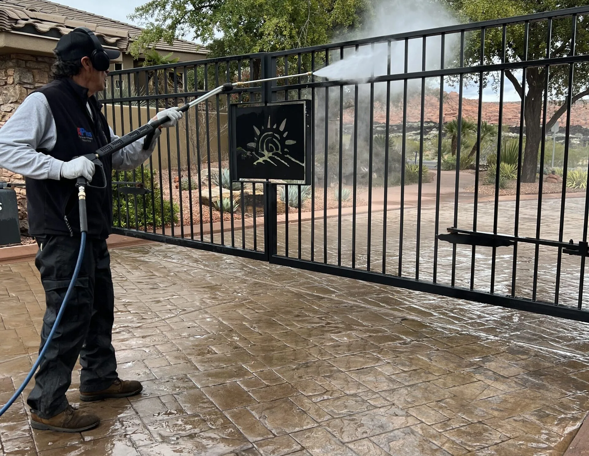 Technician pressure washing a decorative metal driveway gate at a residence