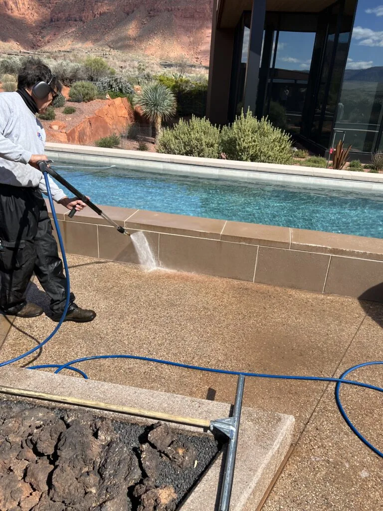 Technician cleaning a stone pool wall and concrete deck at a residential property