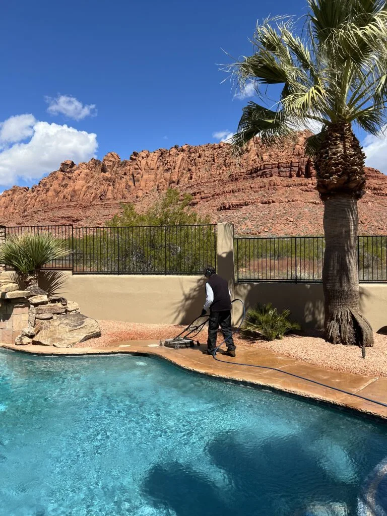 Technician cleaning a concrete pool deck with a surface cleaner and desert red rocks in the background