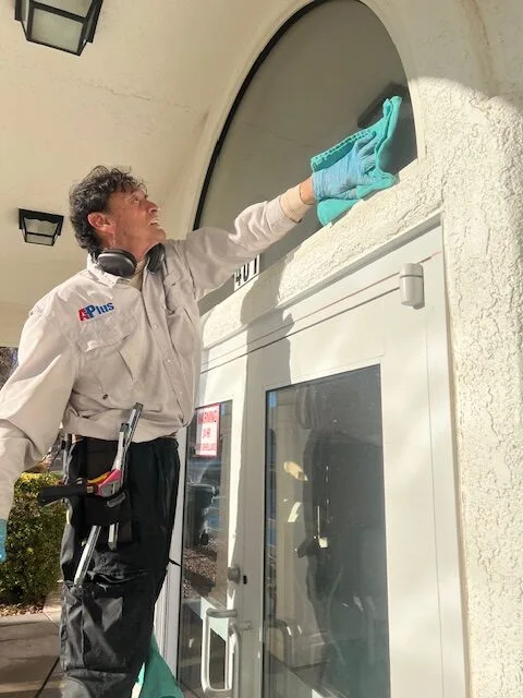A-Plus Power Wash technician cleaning an arched window above an entrance